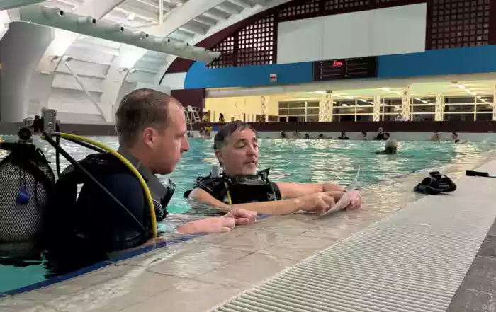 Een kandidaat 1*Duiker krijgt uitleg van een instructeur aan de waterkant - J. Van Laere